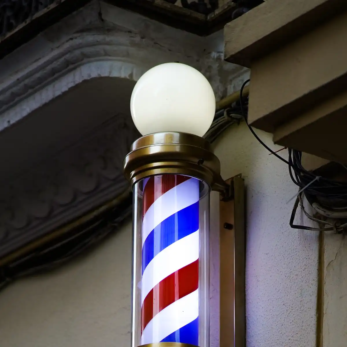 A lit barber's pole with red, white and blue stripes on a building facade at dusk
