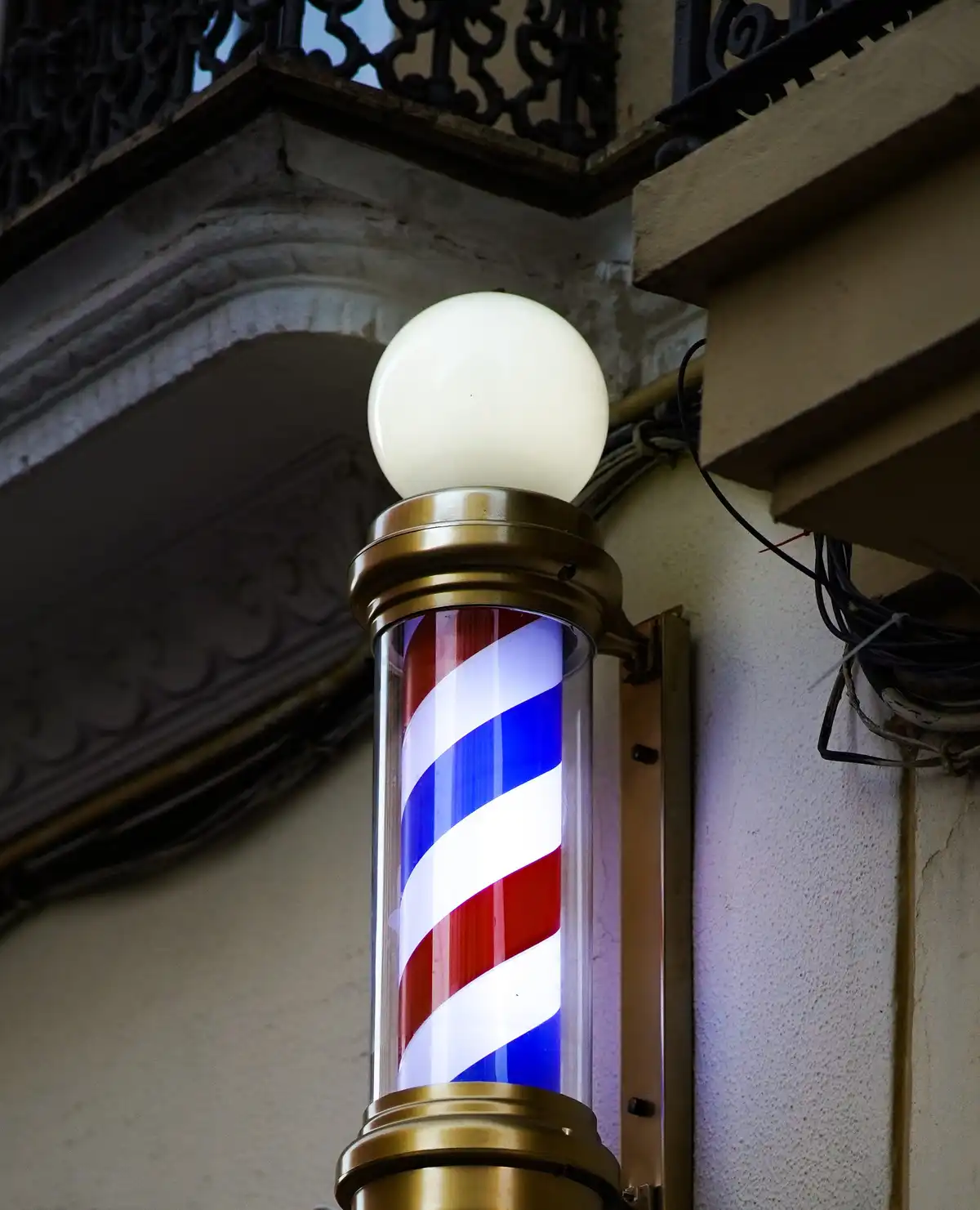 A lit barber's pole with red, white and blue stripes on a building facade at dusk