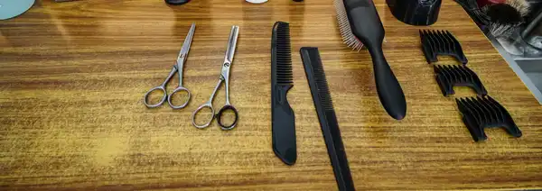Scissors, combs, a brush and clipper guards laid out on a wooden barber's counter