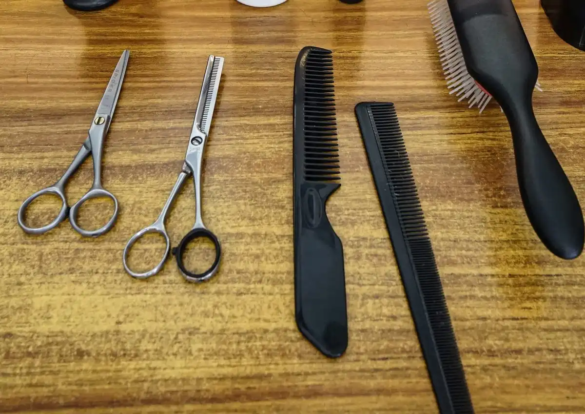 Scissors, combs, a brush and clipper guards laid out on a wooden barber's counter